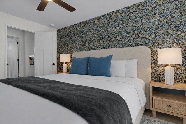 Ein Schlafzimmer mit einem großen Bett, zwei Nachttischen mit Lampen, einem Deckenventilator und einer Wand mit Blumenmuster.