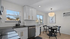 A modern kitchen with white cabinets, a black countertop, and a dining area with a round table and chairs. - Charming 1BR Getaway | Eastpointe (Eastpointe)