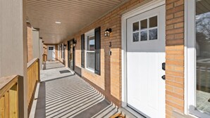 A covered porch with a wooden railing, a brick exterior, and a white door with a window. - Charming 1BR Getaway | Eastpointe (Eastpointe)