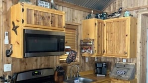 A compact kitchen with wooden cabinets, a microwave, a stove, and a sink. - Cozy 1-bedroom cabin in lovely Rising Star with AC (Rising Star)