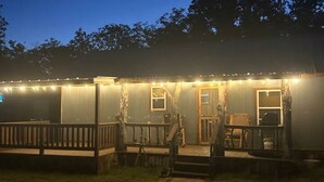 A wooden cabin with a porch, string lights, and a small deck area. - Cozy 1-bedroom cabin in lovely Rising Star with AC (Rising Star)