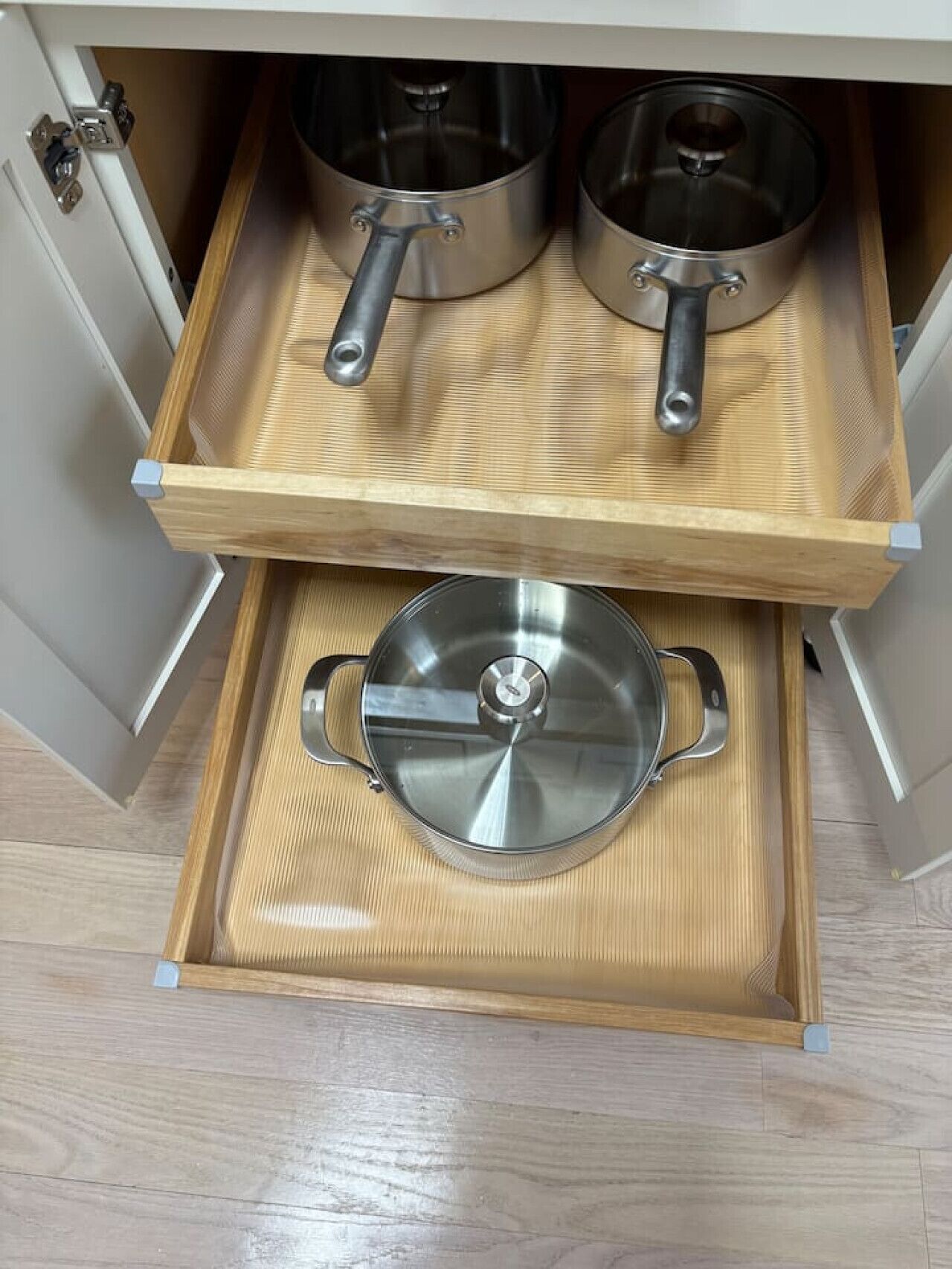 A kitchen drawer with two stainless steel pots and a glass lid.
