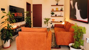 A living room with a TV displaying 'NETFLIX', a sofa, a coffee table, and two potted plants. - Modern, Spacious Apartment — Your Home Away From Home (Dar es Salaam)