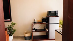 A compact kitchen with a microwave, a small refrigerator, a wooden shelf, and a potted plant. - Modern, Spacious Apartment — Your Home Away From Home (Dar es Salaam)
