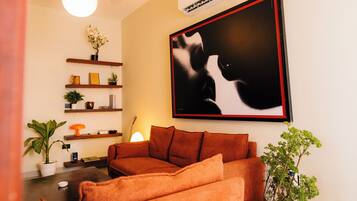 Ein Wohnzimmer mit einer Couch, einer Topfpflanze, einer Lampe und einem gerahmten Bild an der Wand.