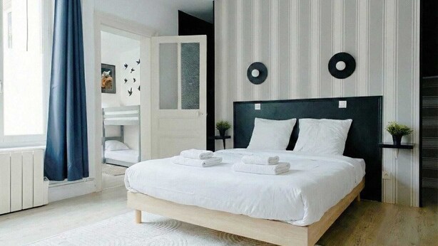 A modern bedroom with a large bed, a bedside table, a mirror, and a window with curtains. - L'Écrin d'Opale: Historic Suite 60m² • King Size Bed • Old Town (Boulogne-sur-Mer)