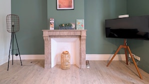 A room with a fireplace, a framed picture above it, a television on a stand, and a floor lamp. - L'Écrin d'Opale: Historic Suite 60m² • King Size Bed • Old Town (Boulogne-sur-Mer)