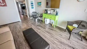Une pièce avec un plancher en bois, un bureau vert avec une chaise, une petite table avec des chaises, un grand miroir et un tableau encadré accroché au mur.
