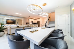 A modern kitchen with white cabinets, a large island, and a dining area with a white table and grey chairs. - Storey Lake 9BR Home w/ Pool & Epic Game Room (Kissimmee)