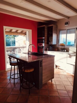 A kitchen with a central island, bar stools, a window with a view, and a red wall. - Air-conditioned house with garden and private pool near Avignon and Pont du Gard (Tavel)
