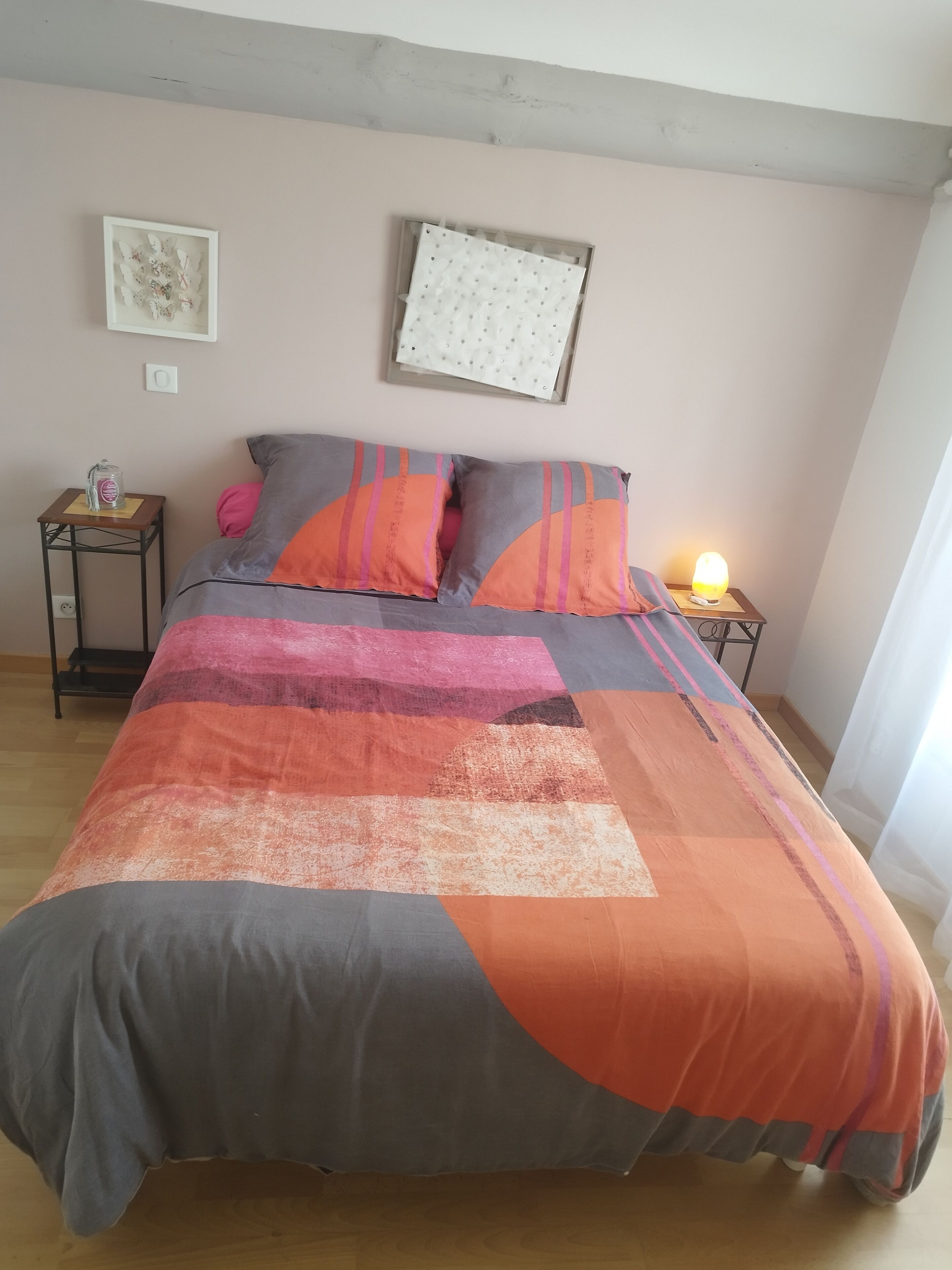 A bed with a colorful quilt, a nightstand with a lamp, and a wall clock.