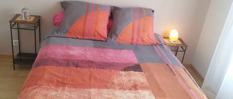 A bed with a colorful quilt, a nightstand with a lamp, and a wall clock.
