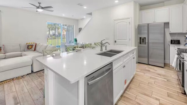 A modern kitchen with white cabinetry, a central island with a sink, and a stainless steel refrigerator. - Cozy villa in Margaritaville Orlando, near Disney, SeaWorld, Universal (Kissimmee)