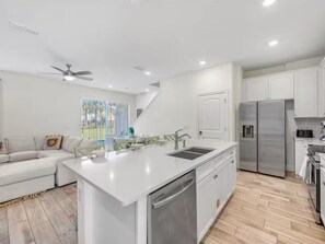 A modern kitchen with white cabinetry, a central island with a sink, and a stainless steel refrigerator. - Cozy villa in Margaritaville Orlando, near Disney, SeaWorld, Universal (Kissimmee)