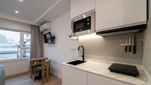 Una cocina moderna con microondas integrado, un lavabo y una encimera con placa de inducción negra. Hay una pequeña mesa de madera y sillas, y una ventana con vistas a edificios.