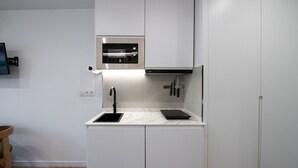 Una cocina moderna con armarios blancos, horno de acero inoxidable, grifo negro y encimera de mármol.