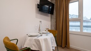 A dining area with a table set for two, a bottle of water, and a glass of wine. A television is mounted on the wall above the table. - 306 — SB20 Boutique Studios | 1BR | 1BA | W/K (Madrid)