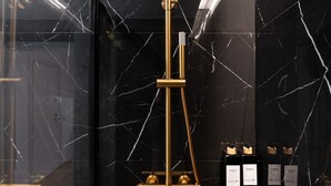 A modern bathroom with a gold showerhead, marble walls, and a toilet. - 306 — SB20 Boutique Studios | 1BR | 1BA | W/K (Madrid)