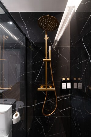 Ein modernes Badezimmer mit Duschbrause in Gold, Marmorwänden und Toilette.