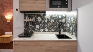 A modern kitchen with a wooden countertop, a black sink, a microwave above, and a floral backsplash. - 306 — SB20 Boutique Studios | 1BR | 1BA | W/K (Madrid)
