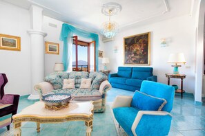 Ein geräumiges Wohnzimmer mit einem großen Fenster, einem blauen Sofa, einem gemusterten Sessel und einem dekorativen Tisch.