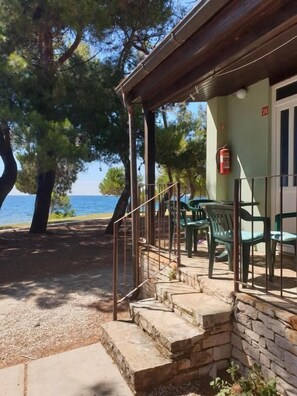A coastal building with a stone staircase leading to a covered porch, outdoor seating, and a fire extinguisher mounted on the wall. - Family Bungalow Pineta (Novigrad)