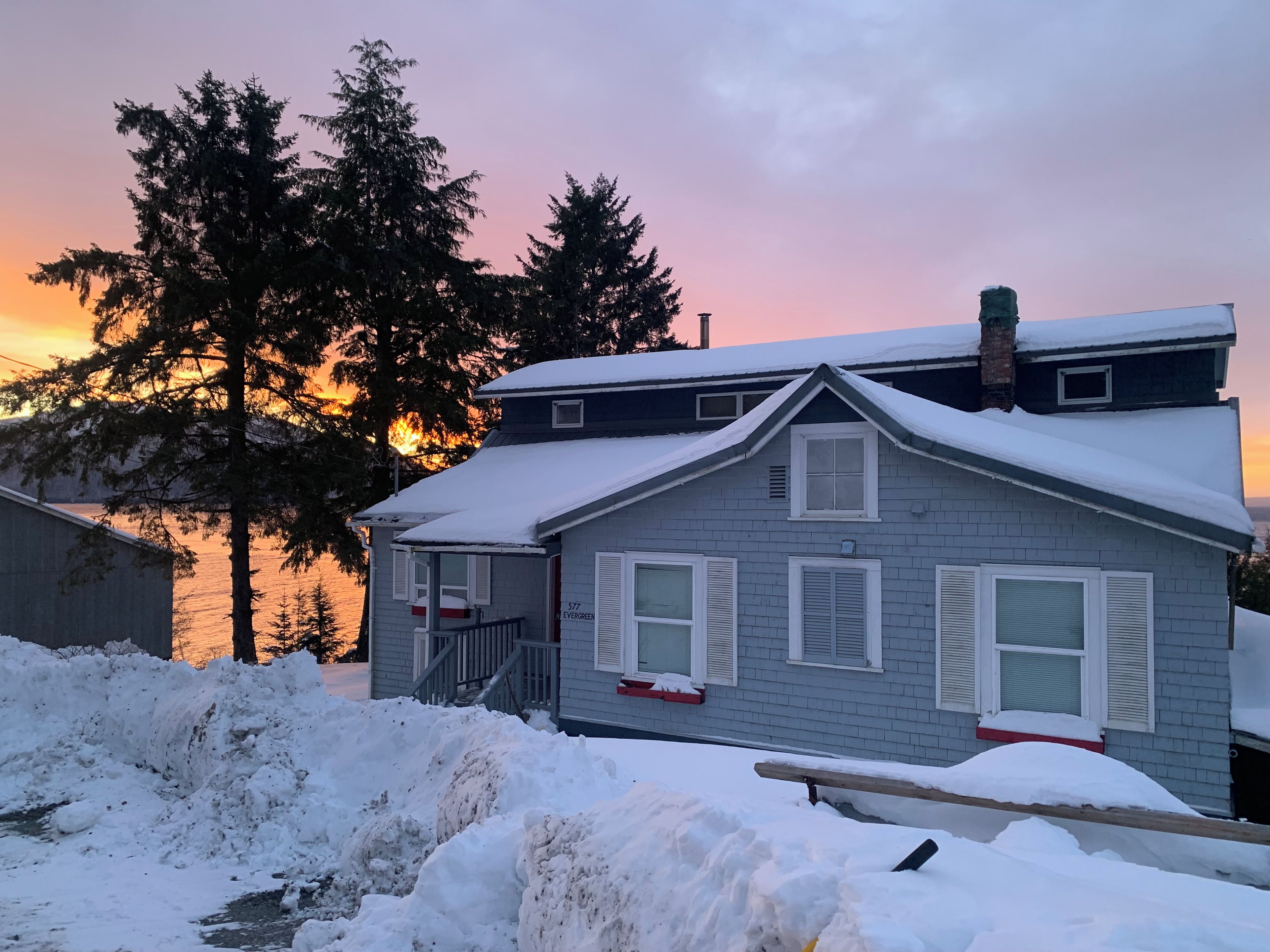 A two-story house with a snow-covered roof and a visible chimney.