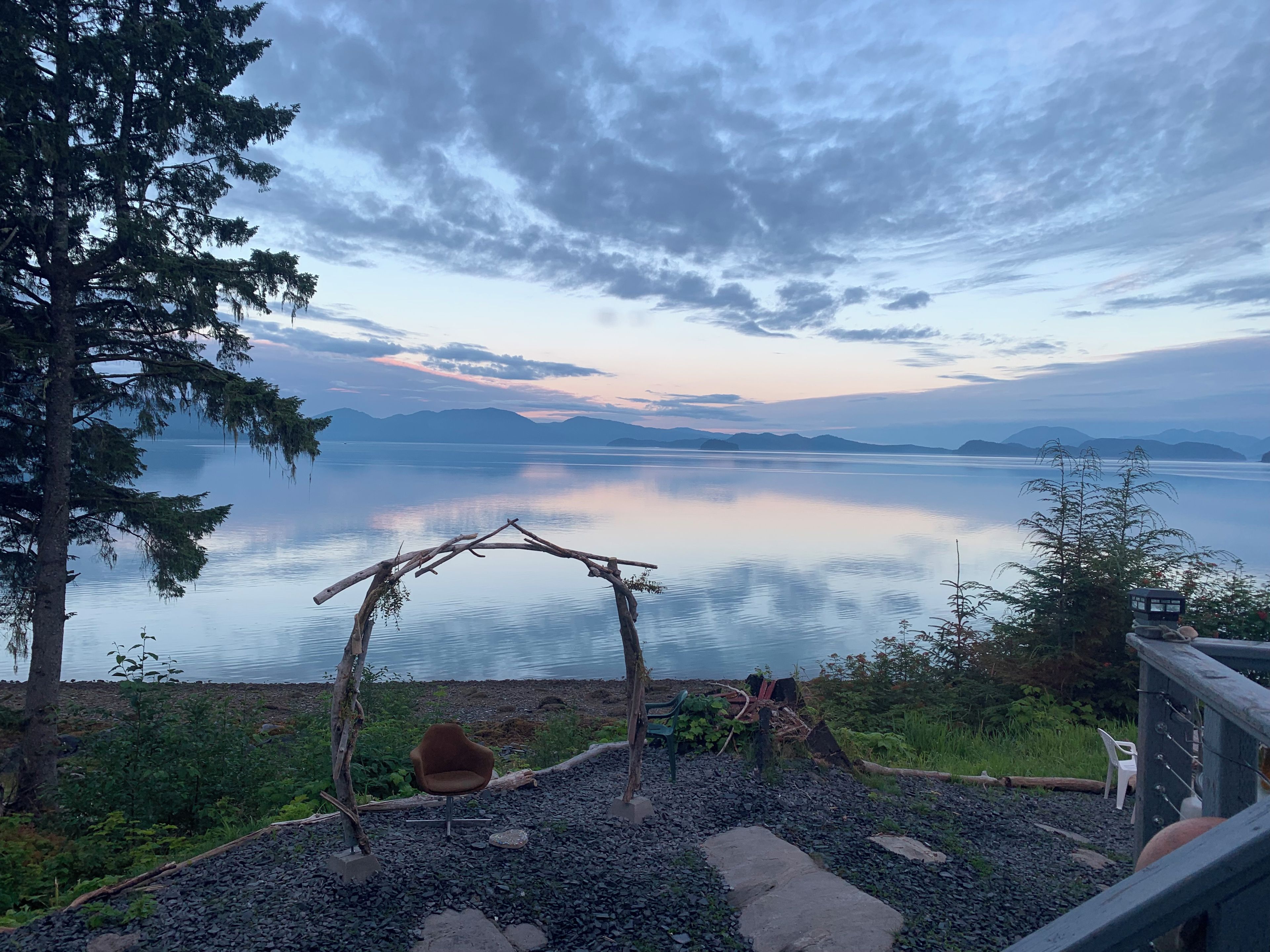 A tranquil lakeside view with a wooden gazebo, a chair, and a rocky foreground.