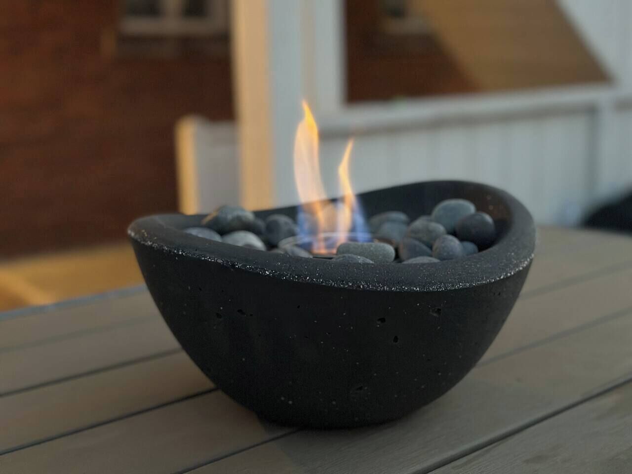 A black bowl-shaped fire pit with a visible flame on a wooden surface.