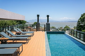 Piscina no terraço com espreguiçadeiras e vista para o mar.