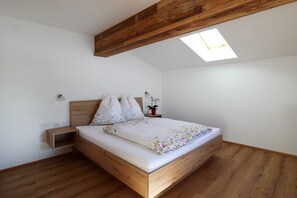 A bedroom with a wooden bed frame, white bedding, a small bedside table, and a skylight. - Leogang: Apartment With Mountain Views (Leogang)