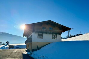 A chalet with a balcony, a ski slope in the background, and a clear sky. - Leogang: Apartment With Mountain Views (Leogang)