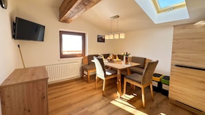 Ein moderner Essbereich mit Holztisch und -stühlen, einem an der Wand montierten Fernseher und einem Oberlicht.