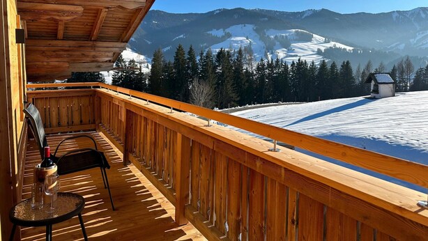 Ein hölzerner Balkon mit Blick auf schneebedeckte Berge und eine kleine Holzhütte.