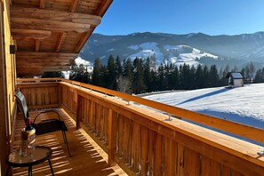 Un balcón de madera con vistas a montañas nevadas y una cabaña pequeña.