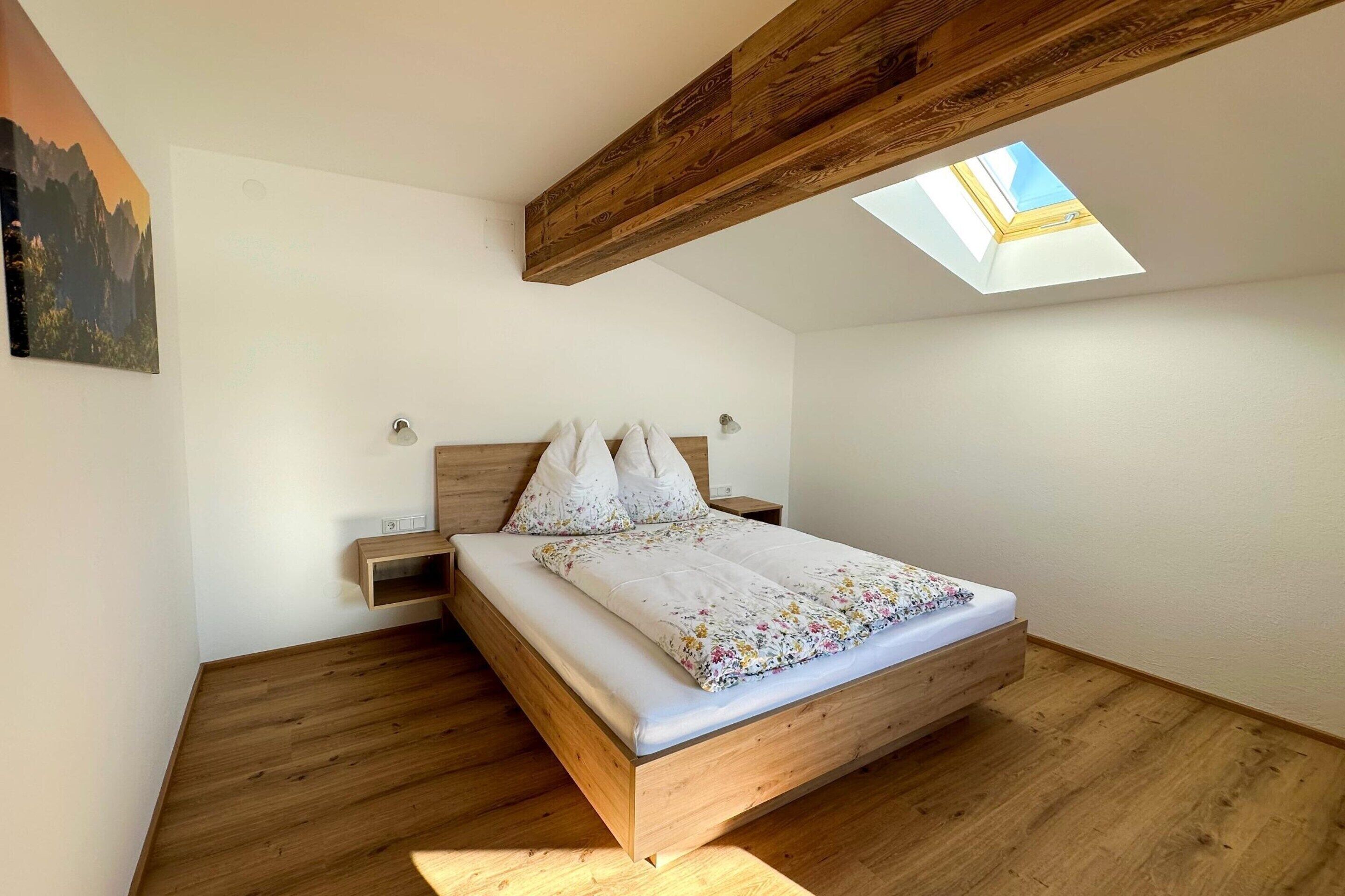 A bedroom with a wooden bed, a skylight, and a small bedside table.