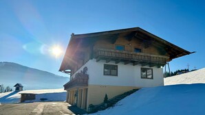 Ein kleines Chalet mit geneigtem Dach, einem Holzbalkon und Blick auf einen verschneiten Berg.
