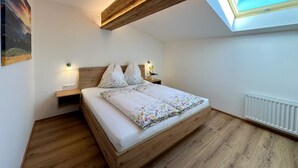 Ein Schlafzimmer mit Oberlicht, Holzbalken, einem Bett mit floralem Bettbezug, Nachttischlampen und einer Heizung.