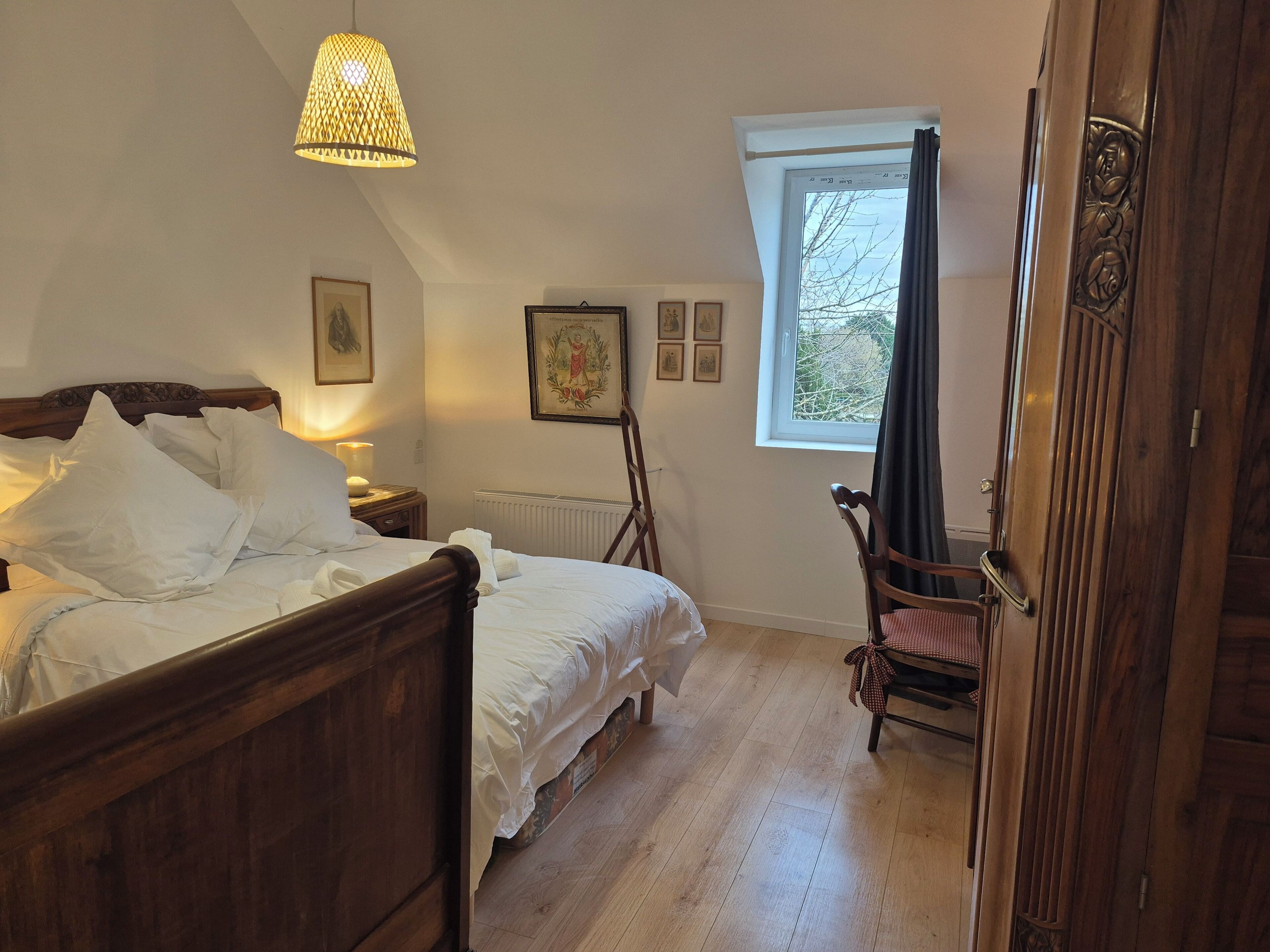 Una camera da letto con un letto di legno, una lampada da terra, un termosifone, una finestra con tende e una porta con pannello decorativo.