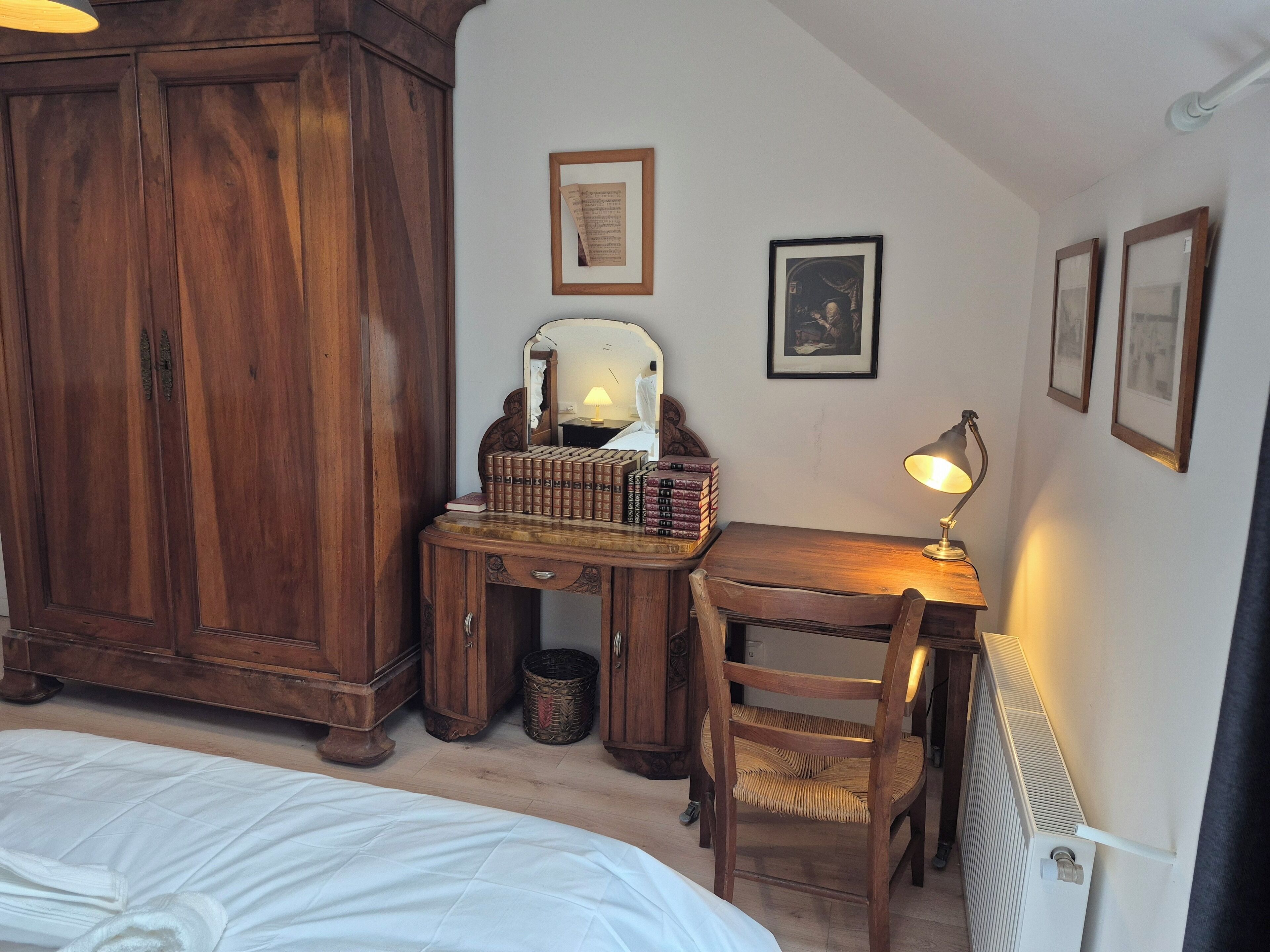 Une chambre avec une armoire en bois, un bureau avec une lampe, une chaise et un lit avec une literie blanche.