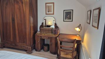 Une chambre avec une armoire en bois, un bureau avec une lampe, une chaise et un lit avec une literie blanche.