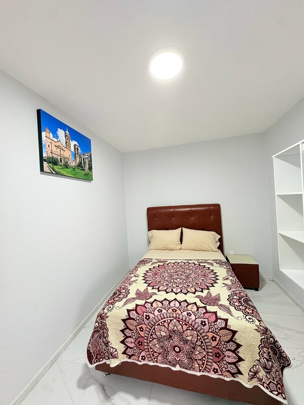 A bedroom with a bed, a nightstand, a wall-mounted shelf, and a painting. - Residencia Gran Coyula Orange 506B (Tonala)