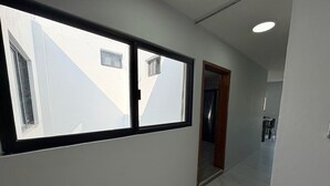 Un couloir avec une grande fenêtre, une porte et un luminaire au plafond.