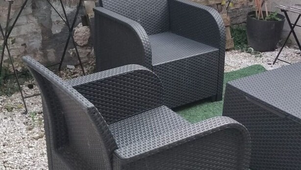 A wicker outdoor seating area with a table and chairs, a stone wall, and a potted plant. - Whole house in town, pets welcome (Caudry)