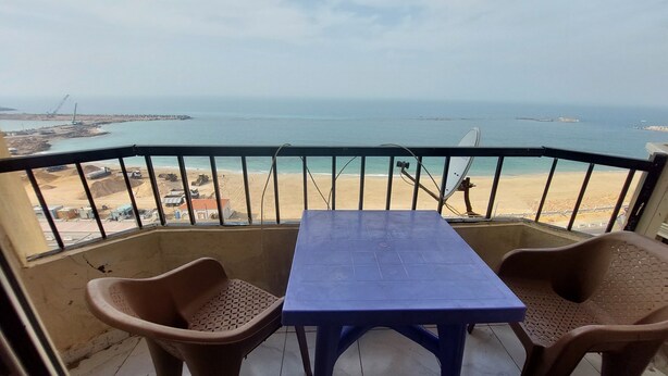 A balcony with a table and two chairs, overlooking a beach and the sea.