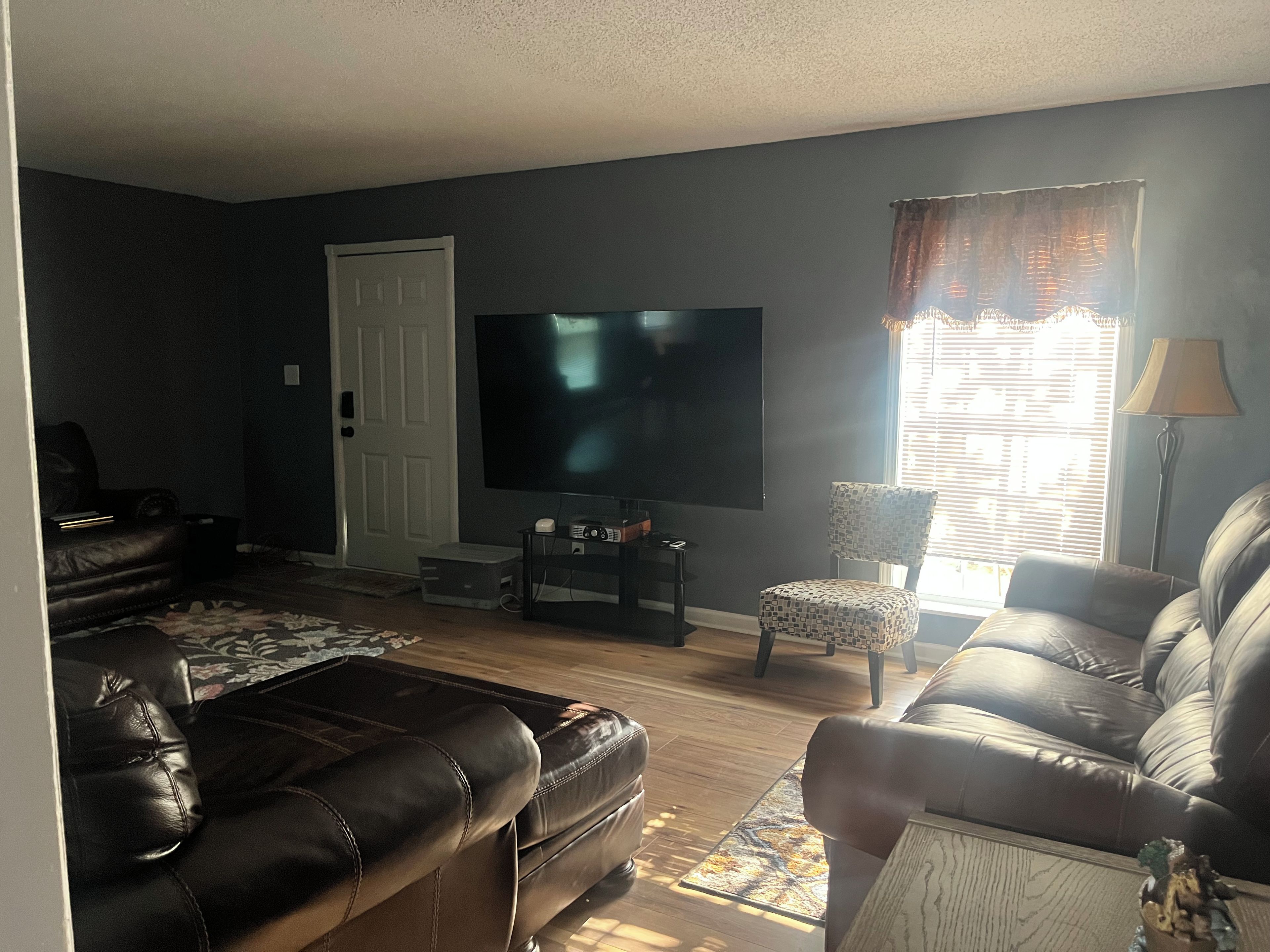 A living room with a flat-screen TV, leather sofas, a patterned rug, and a window with blinds.