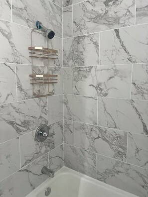 A bathroom with marble tiles, a shower with a handheld showerhead, and a towel rack. - Blues City Nest
A Cozy 2-bedroom 1/12 bath house in central Memphis Tennessee. (Memphis)