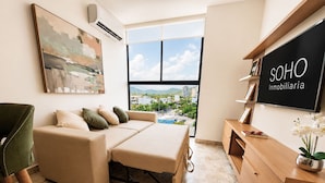 Uma sala de estar moderna com sofá, cama de casal, armário de madeira e uma grande janela com vista para a cidade.