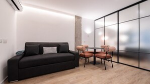 Ein modernes Zimmer mit einer schwarzen Couch, einem kleinen Tisch mit Stühlen und einem großen Fenster mit satinierten Glasscheiben.