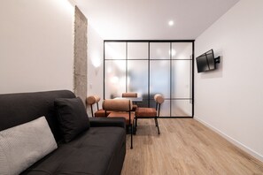 Ein modernes Wohnzimmer mit einer dunklen Couch, einem Couchtisch und einem Essbereich mit Stühlen.